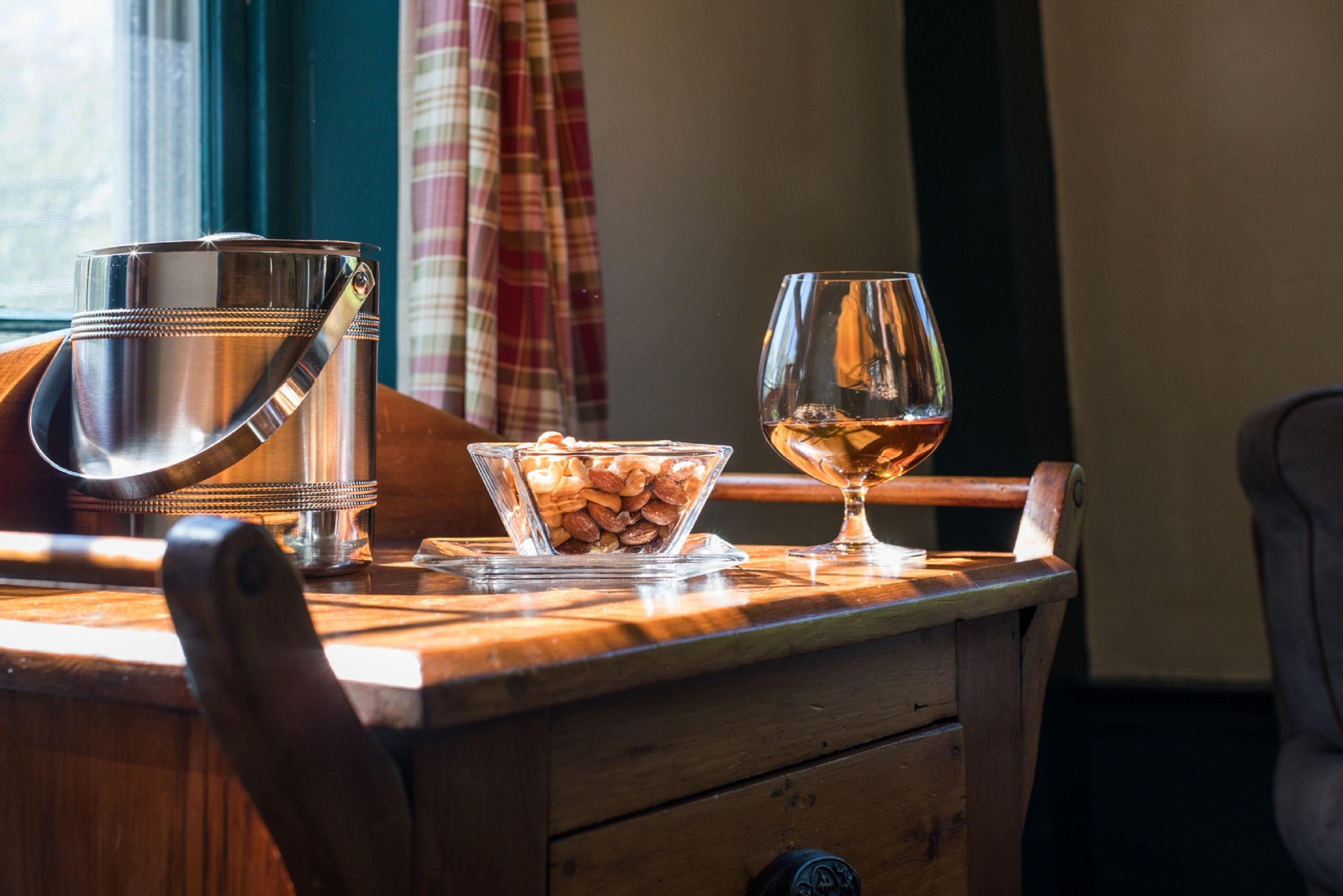Una mesa de madera con un cubo de metal, un cuenco de vidrio con almendras y una copa de vino.
