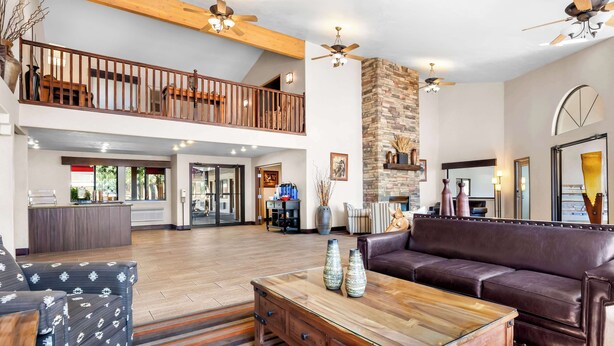 A spacious living area with a high ceiling, a wooden coffee table, a leather sofa, and a staircase leading to an upper level. - Best Western Grande River Inn & Suites (Clifton)