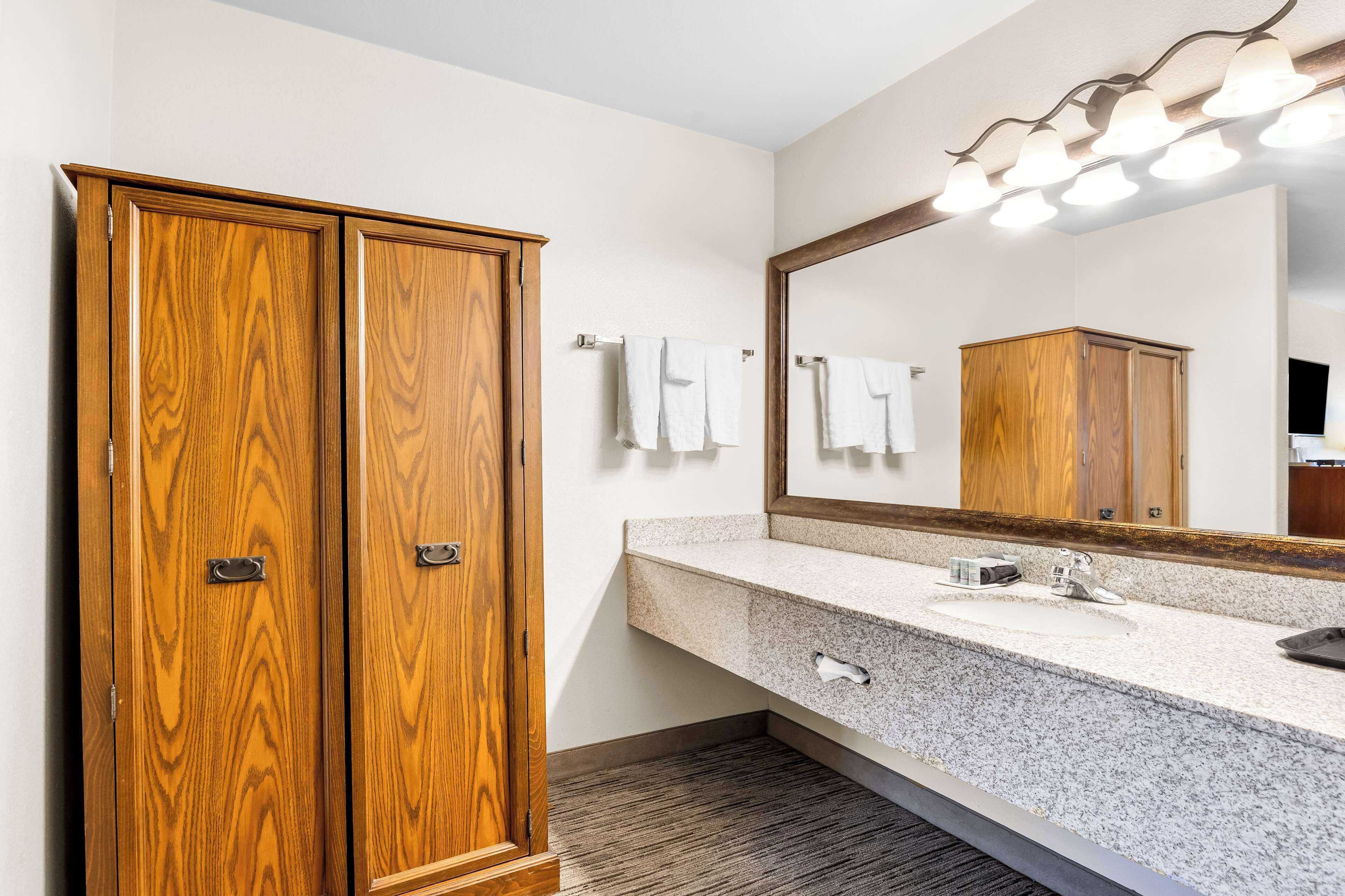 A bathroom with a wooden wardrobe, a granite countertop sink, and a mirror with lights.