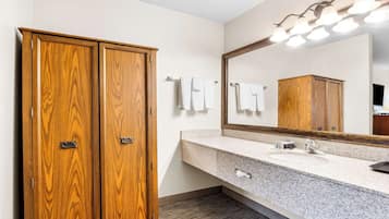 A bathroom with a wooden wardrobe, a granite countertop sink, and a mirror with lights.