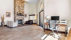 A spacious living room with a stone fireplace, a leather sofa, a desk with a computer, and a large mirror. - Best Western Grande River Inn & Suites (Clifton)