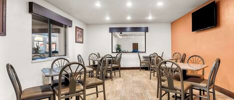 A conference room with multiple tables and chairs, a large window, and a flat-screen TV mounted on the wall.