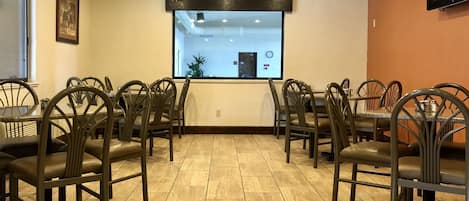 A dining area with multiple tables and chairs, a large window, and a television mounted on the wall.