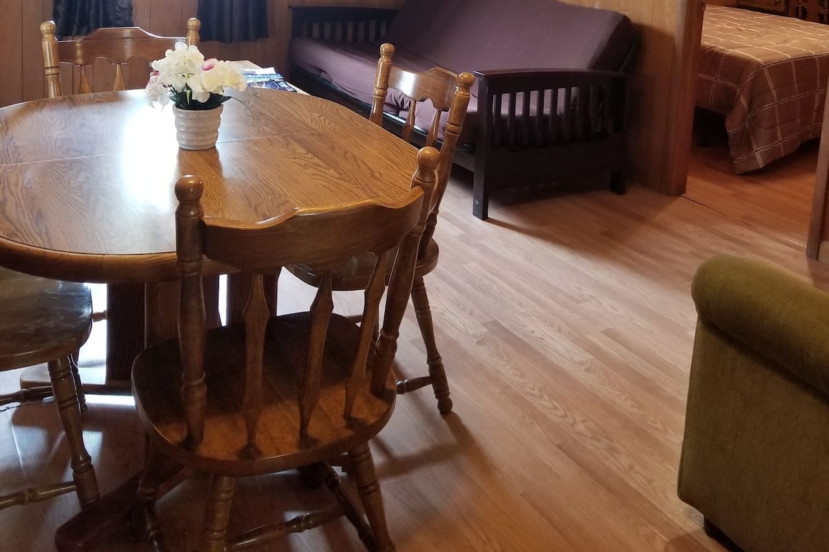 A wooden-paneled room with a dining table, chairs, a sofa, and a bed.