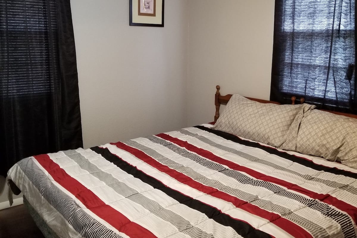 A bedroom with a bed, a ceiling fan, a framed picture on the wall, and a window with curtains.