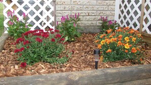 Cama de jardín con flores rojas y anaranjadas, acolchado y un poste de madera.