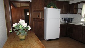 Una cocina con armarios de madera, un refrigerador blanco, un microondas y una mesa de madera con una planta en maceta.