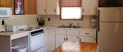 A compact kitchen with wooden cabinets, a white stove, a microwave, and a wooden dining table with benches.