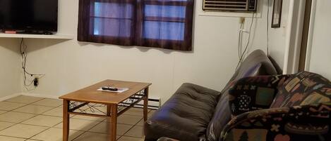 A living room with a sofa, a coffee table, a TV, a window with curtains, and a ceiling fan.