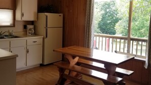 Una cocina con armarios de madera, un refrigerador, una mesa de madera y un ventanal con vista a árboles.