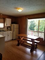Una cocina con armarios de madera, un refrigerador, una mesa de madera y un ventanal con vista a árboles.