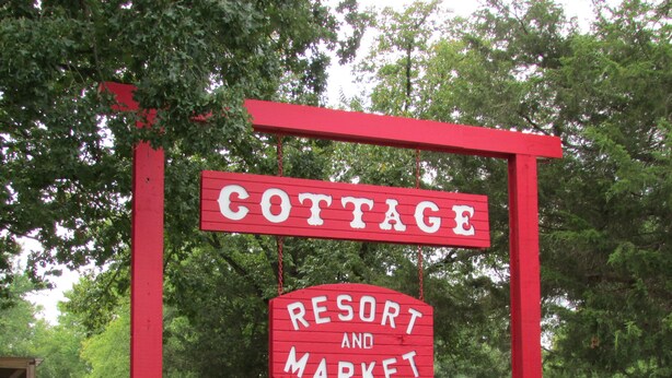Un letrero rojo con letras blancas que dice 'COTTAGE RESORT AND MARKET'.