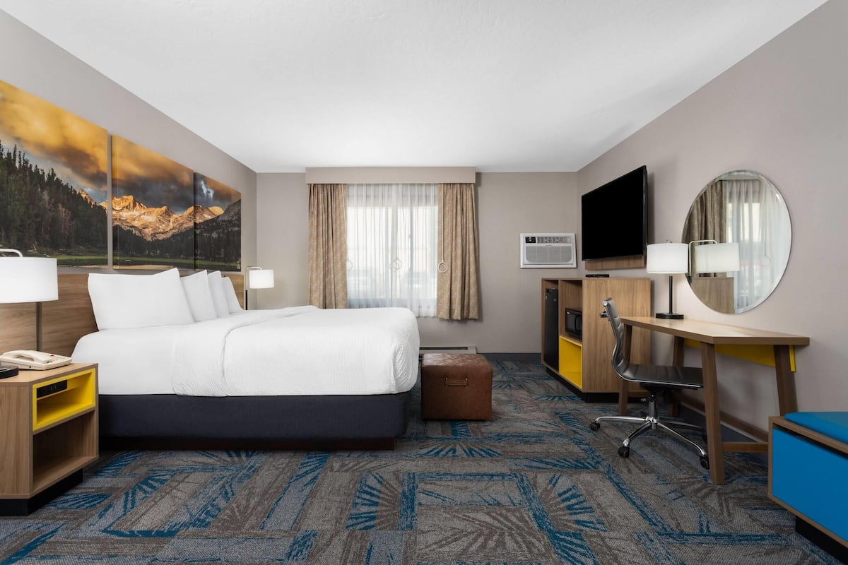 A hotel room with a large bed, a desk with a chair, a television, and a large window with curtains.