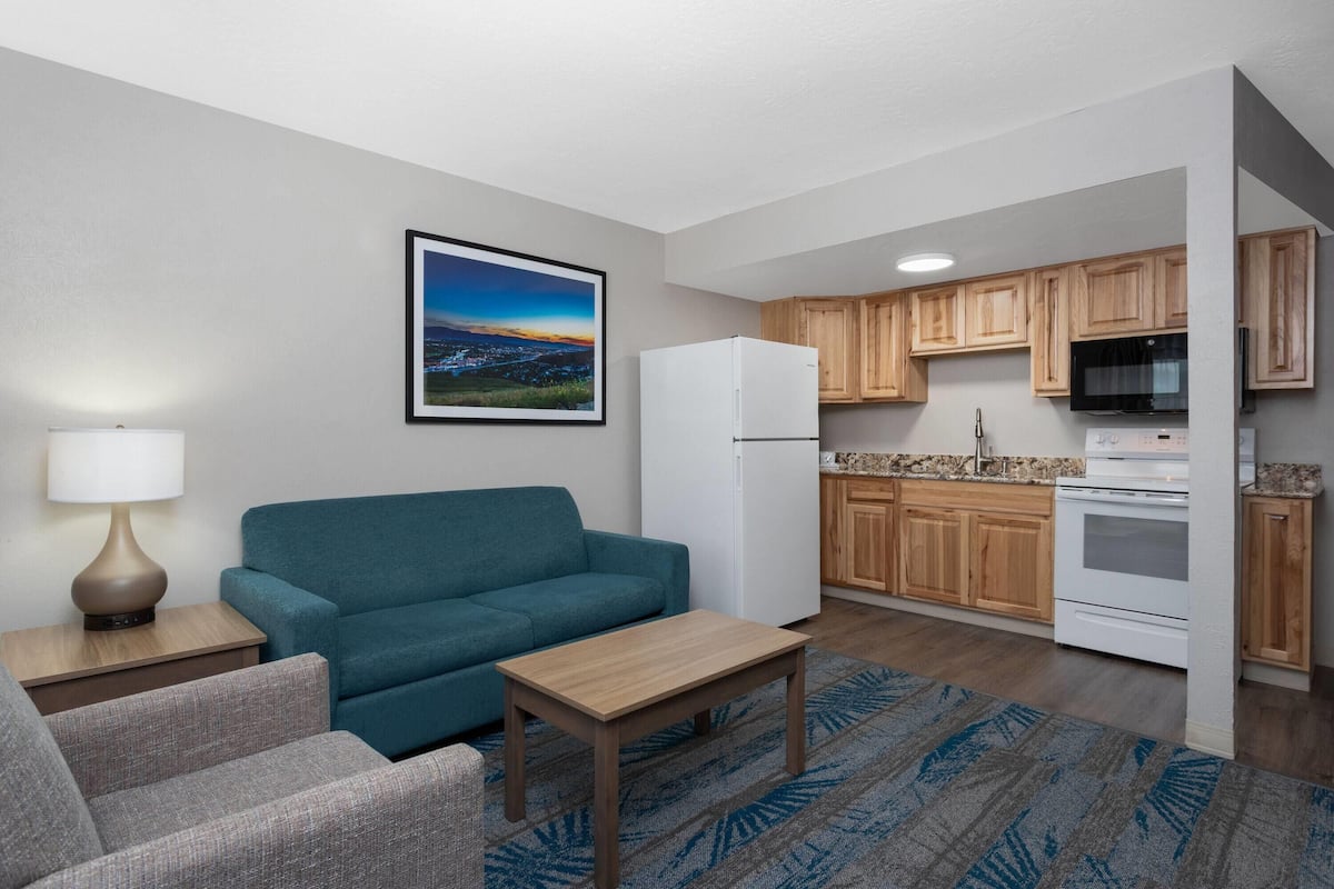 A compact living space with a kitchenette, a blue sofa, a wooden table, and a lamp.