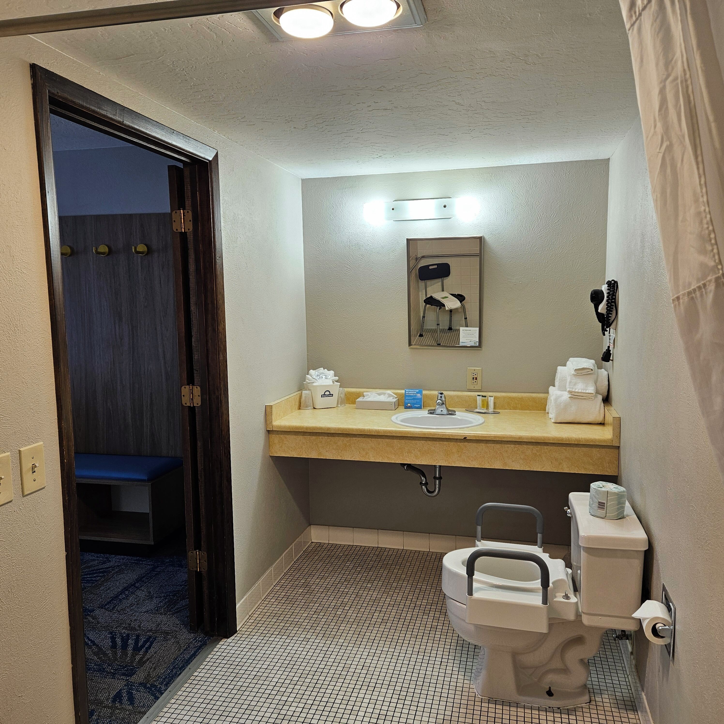 A small bathroom with a sink, toilet, and a mirror. There is a blue bench in the background.