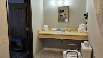 A small bathroom with a sink, toilet, and a mirror. There is a blue bench in the background.