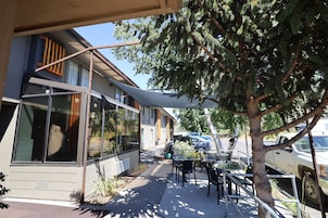 A building with large windows, outdoor seating, and a tree in front.