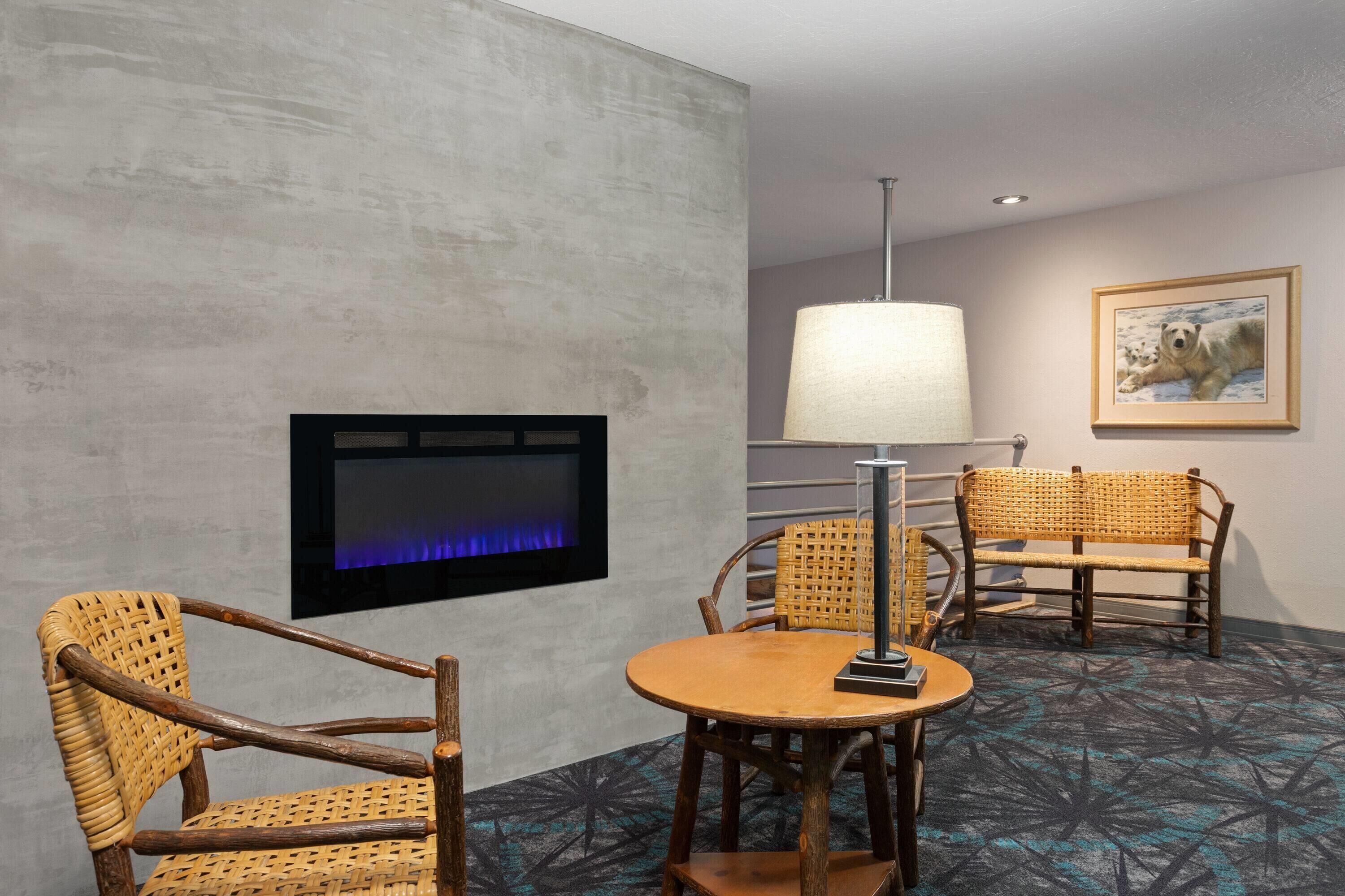 A room with a fireplace, wicker chairs, a round table, a lamp, and a framed picture on the wall.
