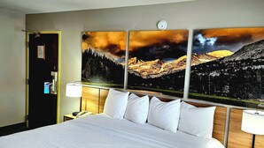 A hotel room with a large bed, a nightstand with a lamp, and a painting of a mountain landscape on the wall.