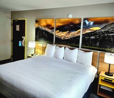 A hotel room with a large bed, a nightstand with a lamp, and a painting of a mountain landscape on the wall.