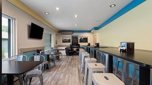 A restaurant with high tables and stools, a flat-screen TV mounted on the wall, and a bar area with stools.