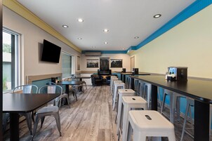 A restaurant with high tables and stools, a flat-screen TV mounted on the wall, and a bar area with stools.