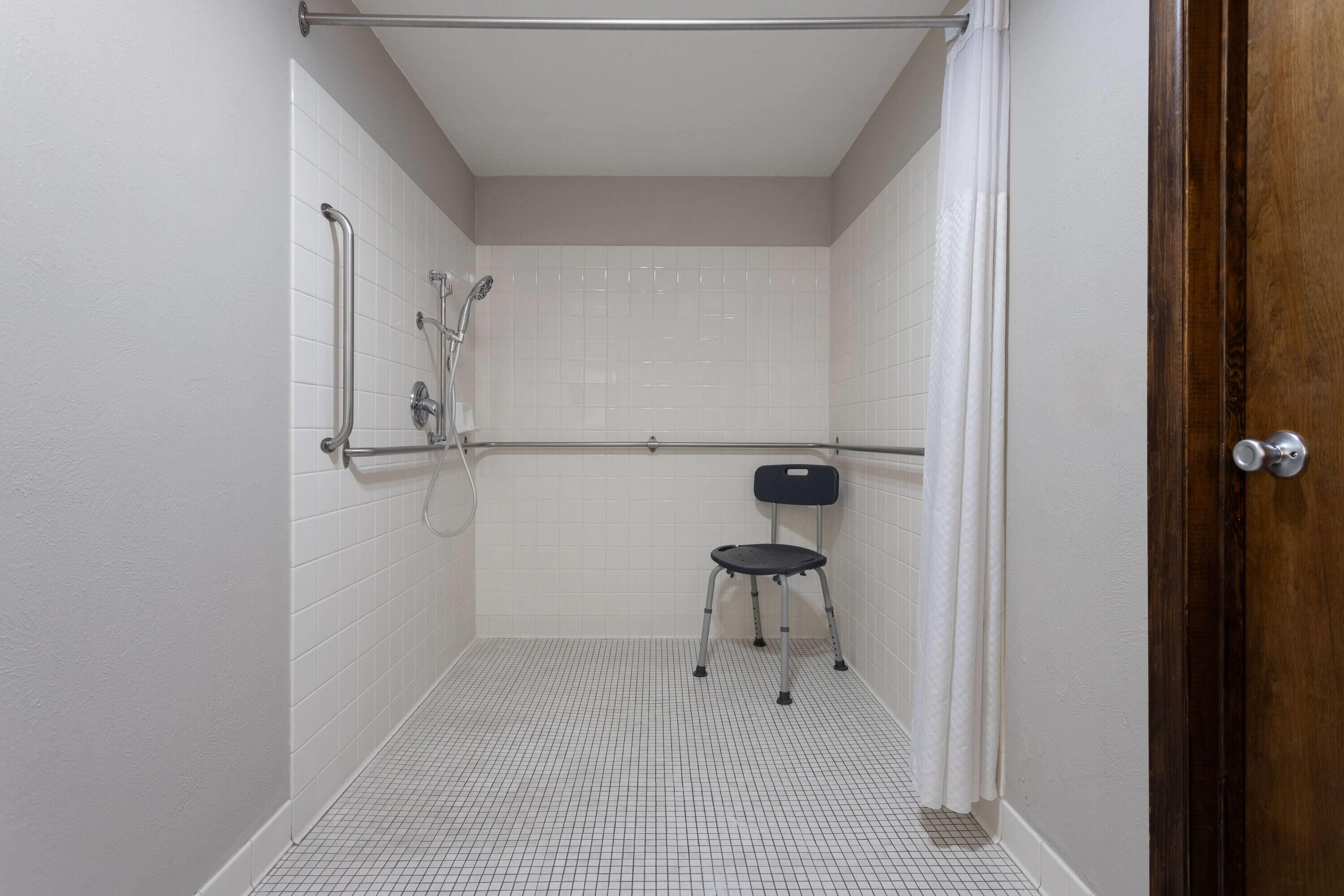 Une petite salle de bain carrelée, équipée d’une douche, de toilettes et d’une chaise.