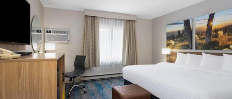 Habitación de hotel con cama, escritorio, silla, televisor, aire acondicionado y ventana con cortinas.