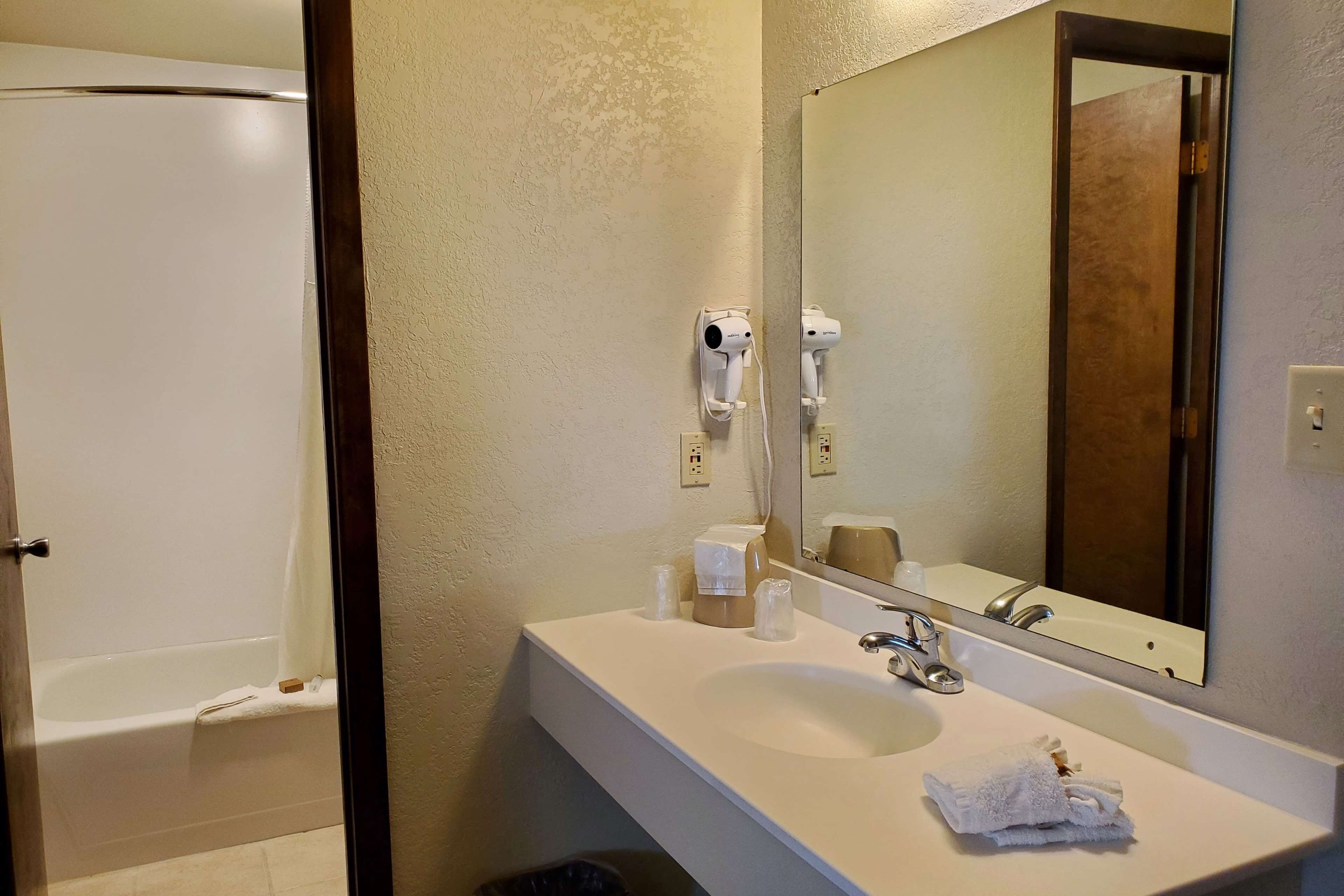 A bathroom with a white sink, a mirror, a hairdryer, and a shower.