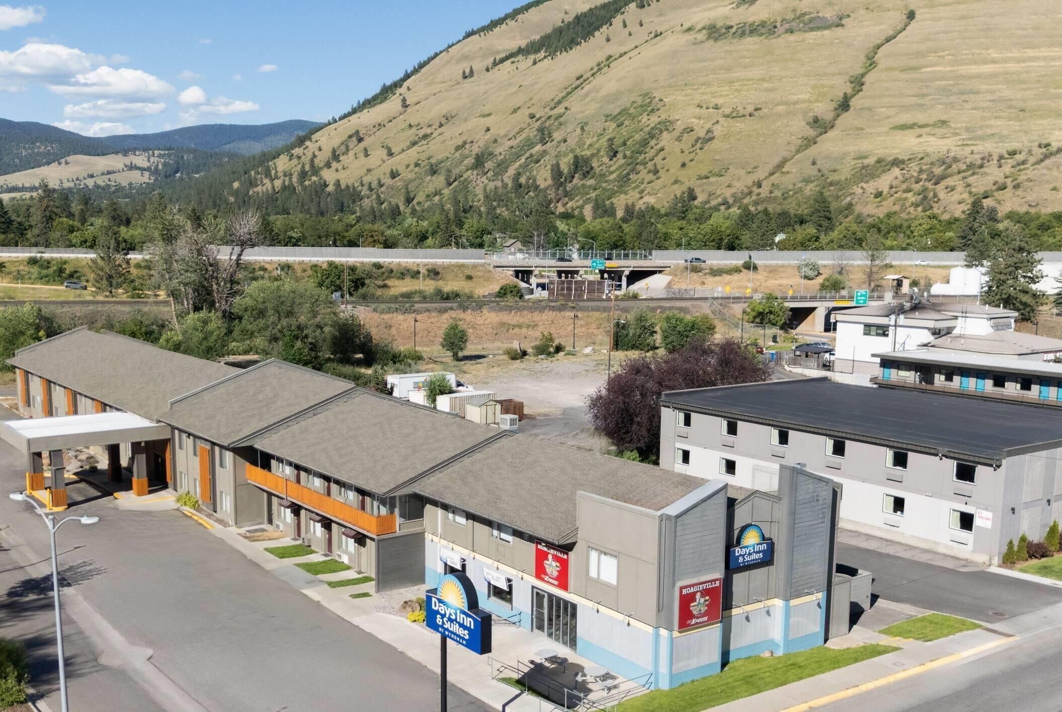 A Days Inn & Suites hotel with a parking lot, a road, and a mountainous landscape in the background.