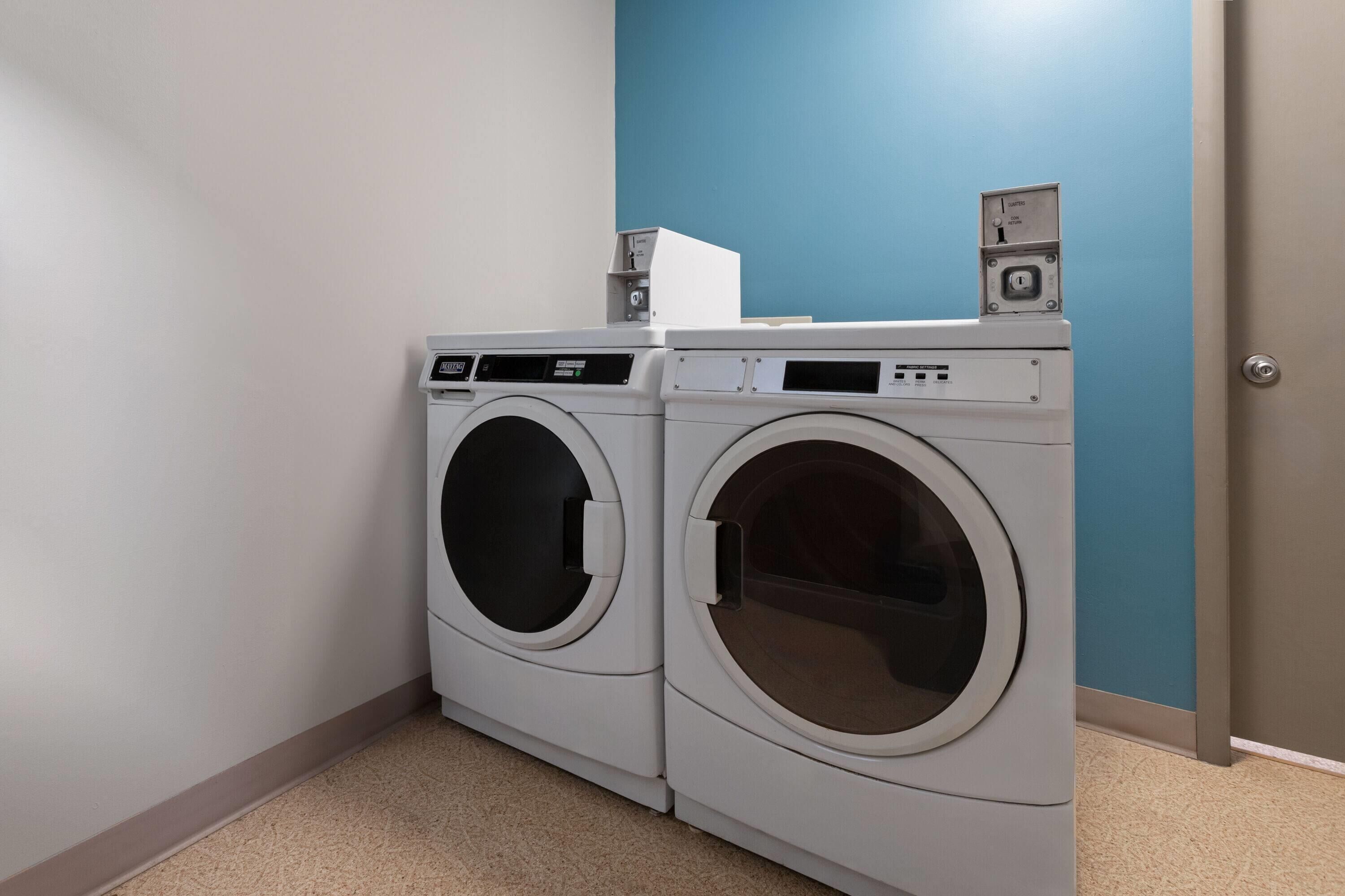 A laundry room with two front-loading washing machines, a control panel, and a small electrical box on top.