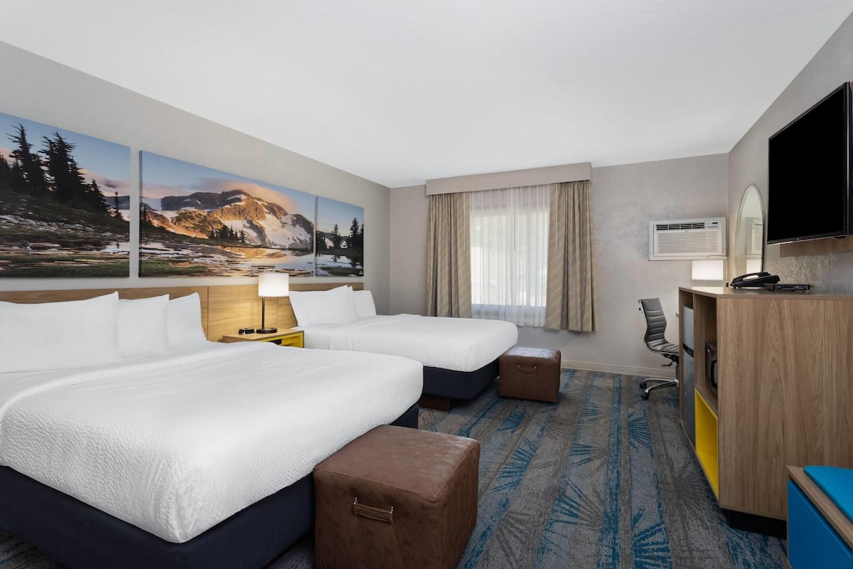 A hotel room with two beds, a desk, a chair, a TV, and a large window with curtains.