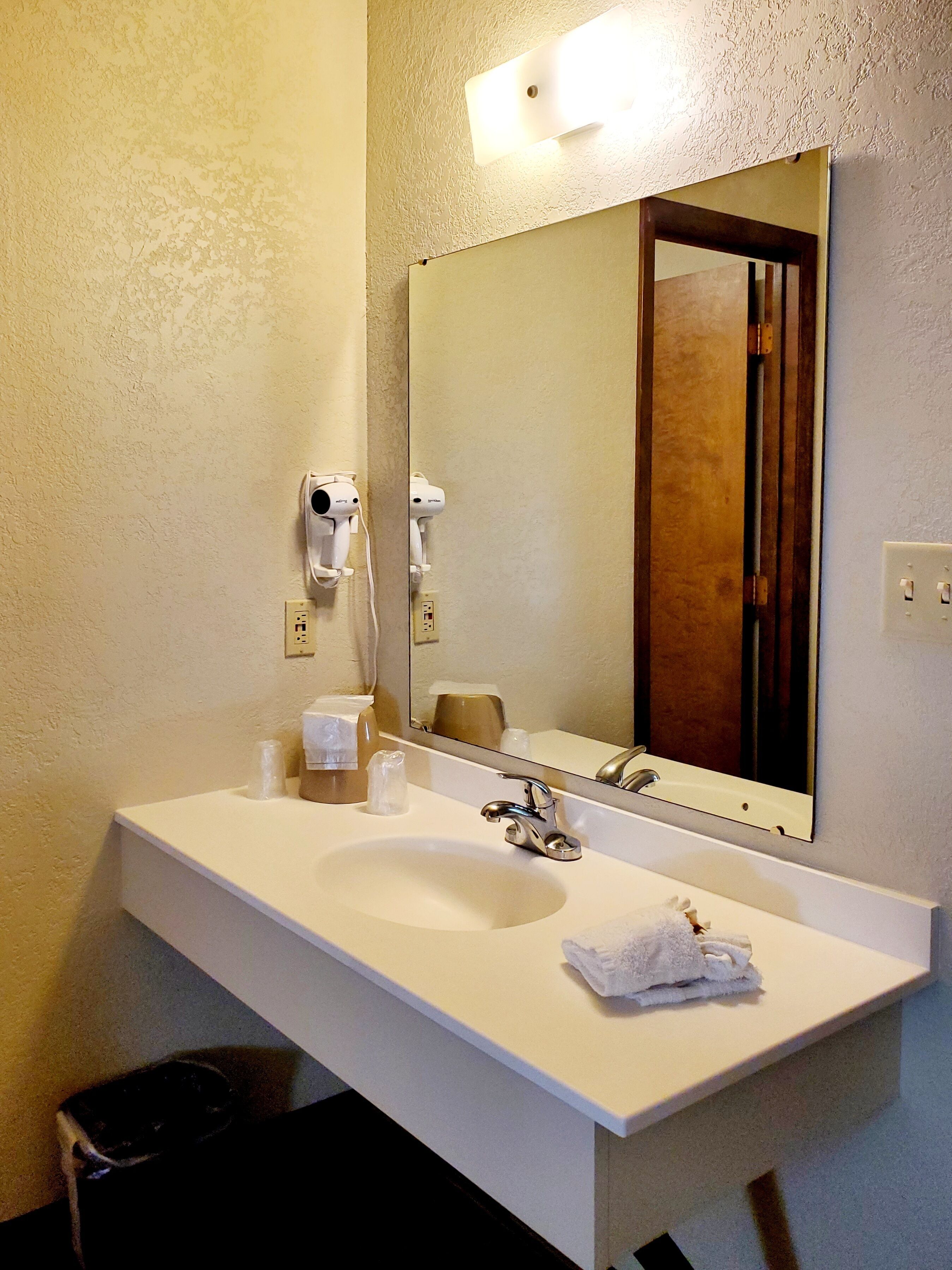 Un baño con un lavamanos blanco, un espejo y un secador de pelo montado en la pared.