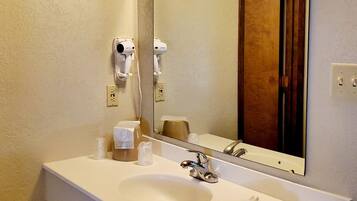 Un baño con un lavamanos blanco, un espejo y un secador de pelo montado en la pared.