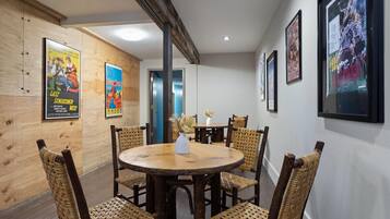 A dining area with a round wooden table and wicker chairs, surrounded by wooden panel walls with posters.