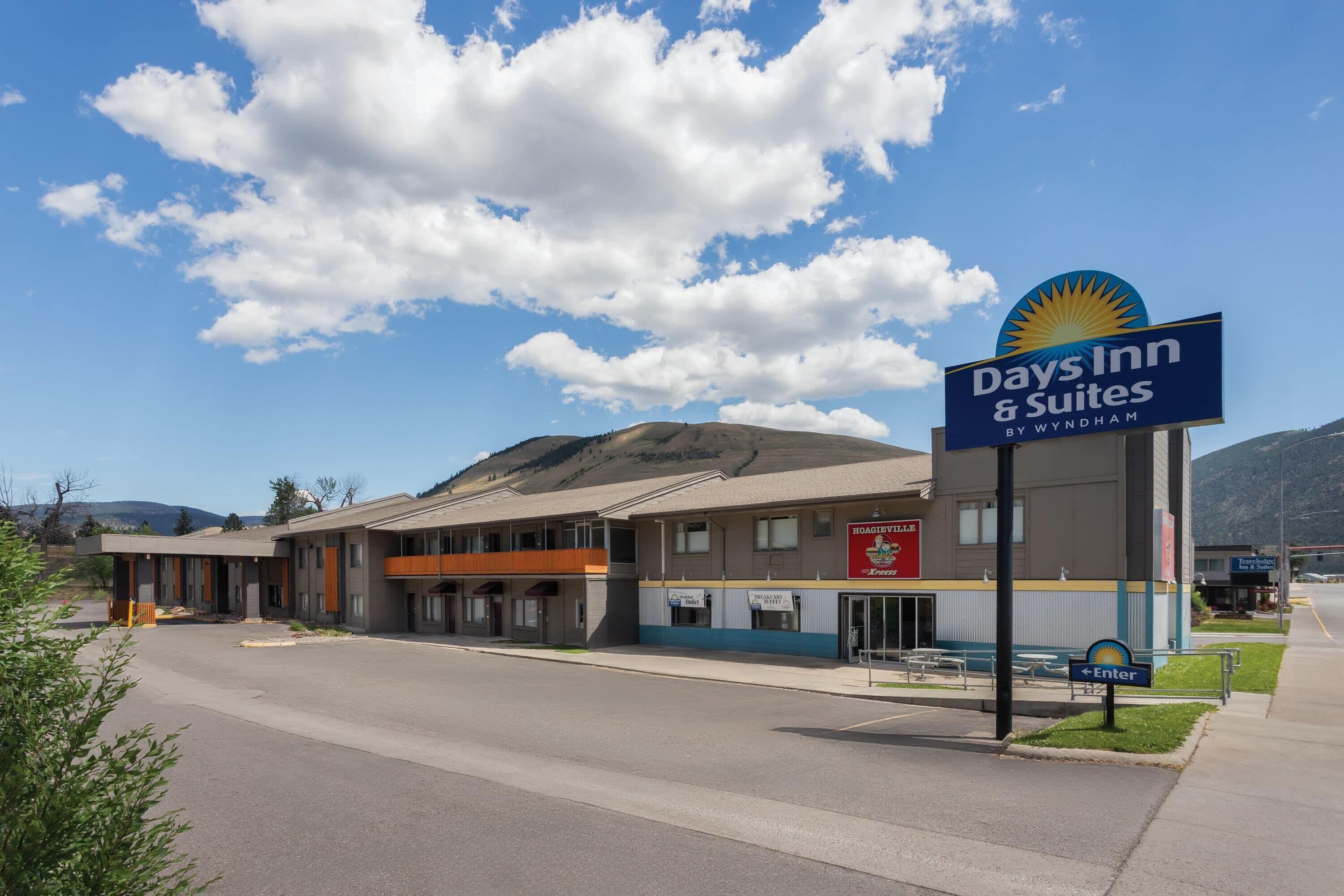 A Days Inn & Suites by Wyndham with a signboard, a parking lot, and a mountain in the background.