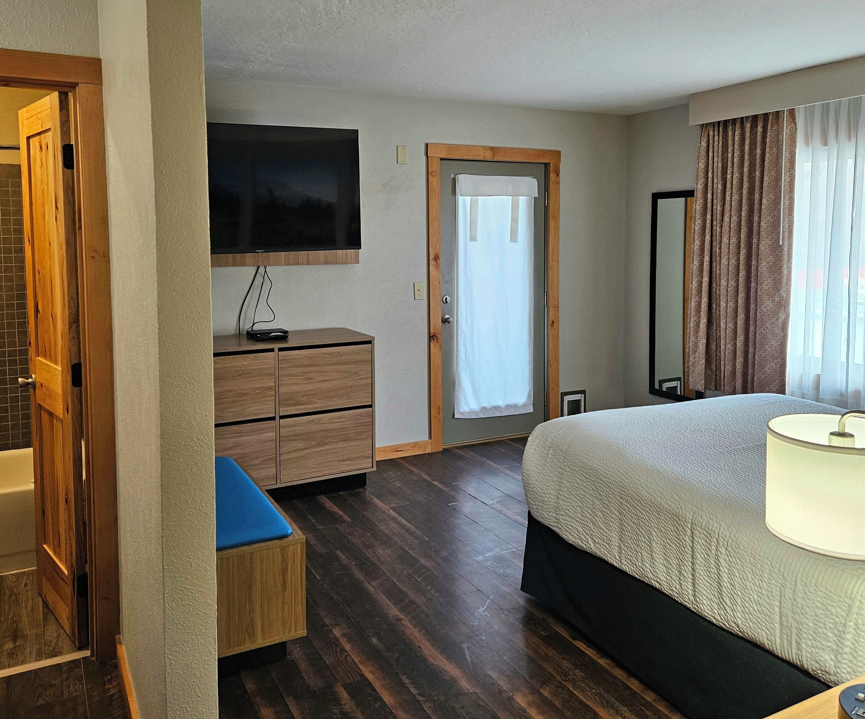 Hotelkamer met een bed, een bureau met stoel, een aan de muur bevestigde televisie, een deur met gordijn en een spiegel.