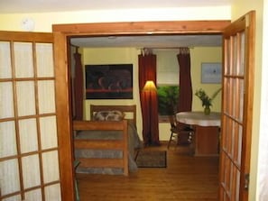 A traditional Japanese-style room with tatami flooring, a low wooden bed, a small table with a lamp, and a painting on the wall.