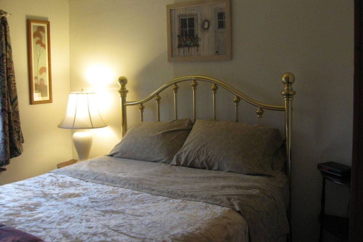 A bedroom with a bed, a bedside lamp, a framed picture on the wall, and a small table with a device.