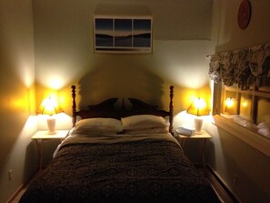 A bedroom with a bed, two bedside lamps, a nightstand, a window with curtains, and a wall-mounted picture. - The Woods Lodge (Northfield)