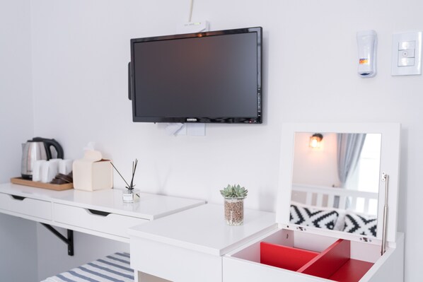 Une chambre d’hôtel moderne équipée d’un téléviseur à écran plat fixé au mur, d’une table de chevet avec un miroir, d’une petite plante en pot et d’une chaise rouge.