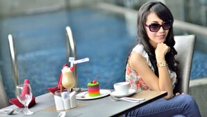 A person seated by a poolside table with a drink, a cake, and a cup. - Serela Waringin (Bandung)