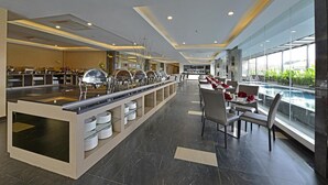 A modern hotel dining area with a buffet setup, a pool view, and a spacious layout. - Serela Waringin (Bandung)