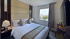 A hotel room with a large bed, a TV, a desk with a chair, and a window with a city view. - Serela Waringin (Bandung)