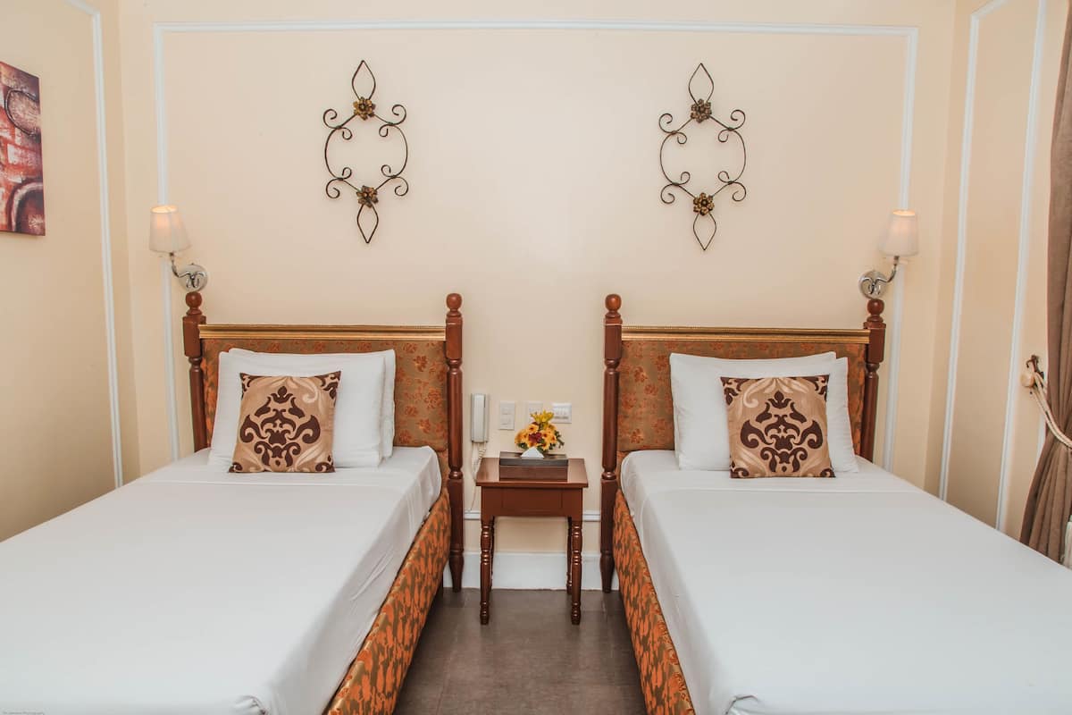 A hotel room with two single beds, a small bedside table with a lamp, and decorative wall sconces.