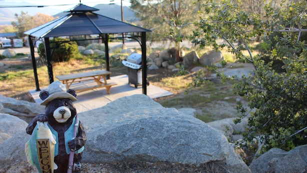 A bear figurine holding a fish with "WELCOME" on it, a gazebo, and a barbecue grill in a park setting.