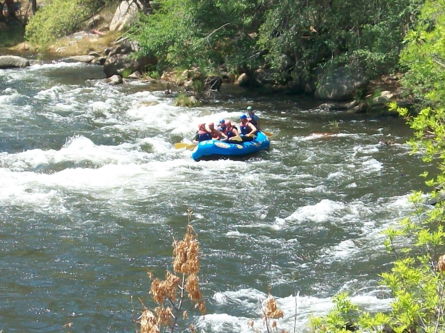A group of people rafting on a river surrounded by rocks and greenery.