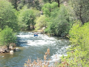 A river with a blue raft navigating through it, surrounded by dense green foliage. - Lakeshore Lodge (Wofford Heights)