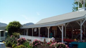 A covered outdoor seating area with a white picket fence, surrounded by flowering plants and a sign indicating a smoking area. - Lakeshore Lodge (Wofford Heights)