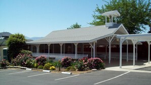 A building with a covered porch, a white picket fence, and a parking lot with marked spaces. - Lakeshore Lodge (Wofford Heights)